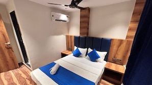 A hotel room with a bed, wooden headboard, nightstands, an air conditioning unit, and a ceiling fan. - Hotel Lavish Park (Mumbai)