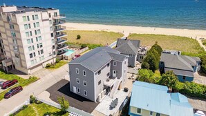 Un quartier résidentiel situé sur la côte, avec un grand immeuble, une maison plus petite et une plage en arrière-plan.