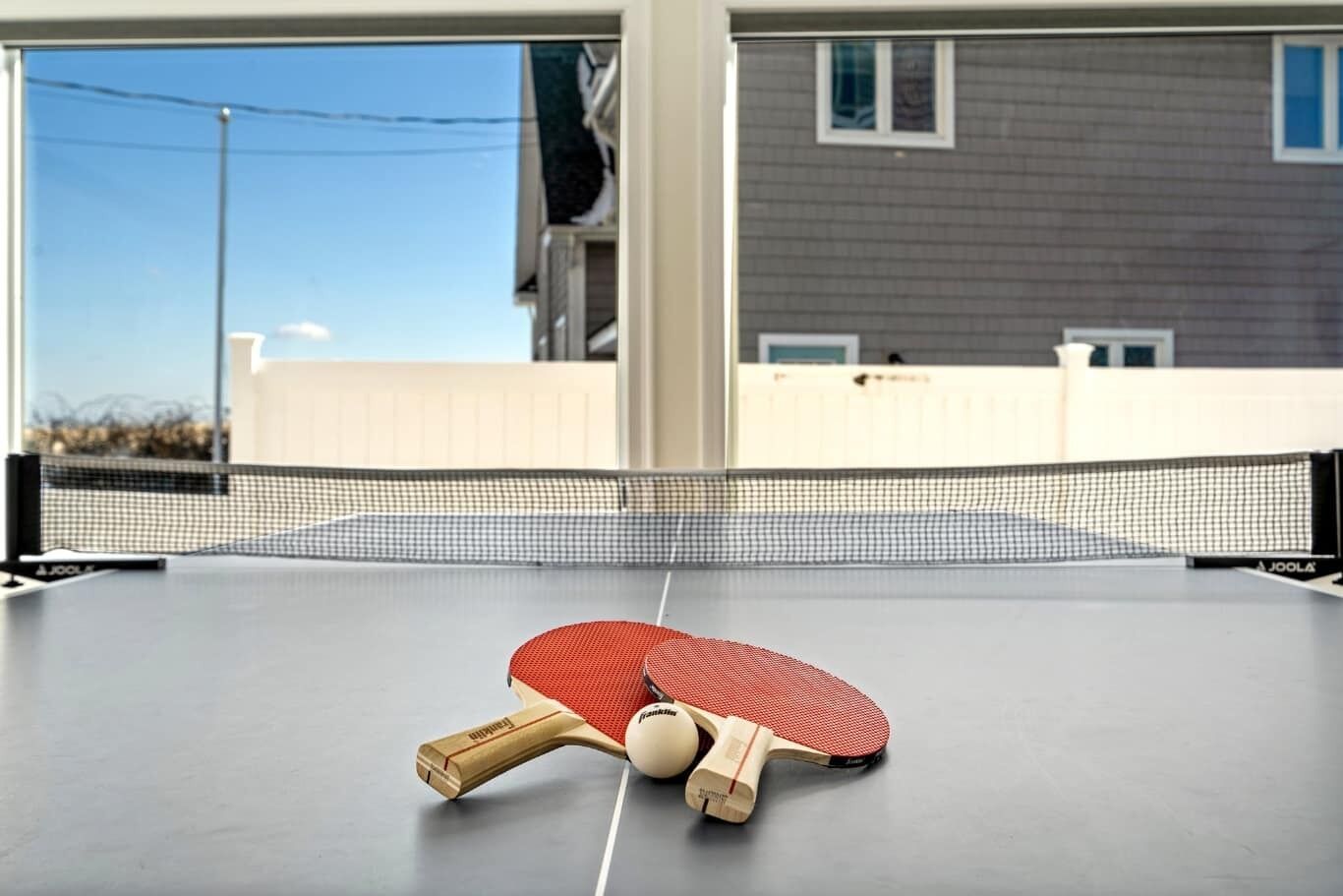 A ping pong table with paddles and a ball, set up outdoors with a building in the background.