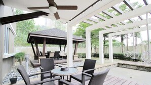 Une terrasse extérieure aménagée avec des meubles en osier, un ventilateur de plafond et une structure en forme de pergola.