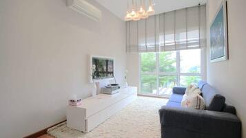 Een moderne woonkamer met een witte tv-kast, een grijze bank en een groot raam met zonwering.