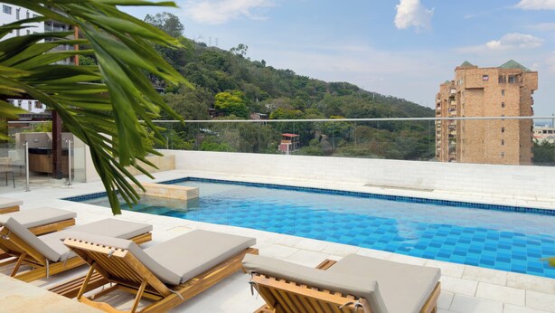 A rooftop pool with lounge chairs and a view of a hillside and a building.