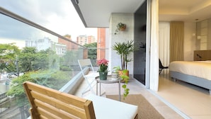 A modern bedroom with a large window, a bed, a chair, and a small table with plants.