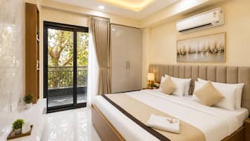 A hotel room with a bed, an air conditioning unit, a ceiling fan, a balcony with curtains, and a painting on the wall.