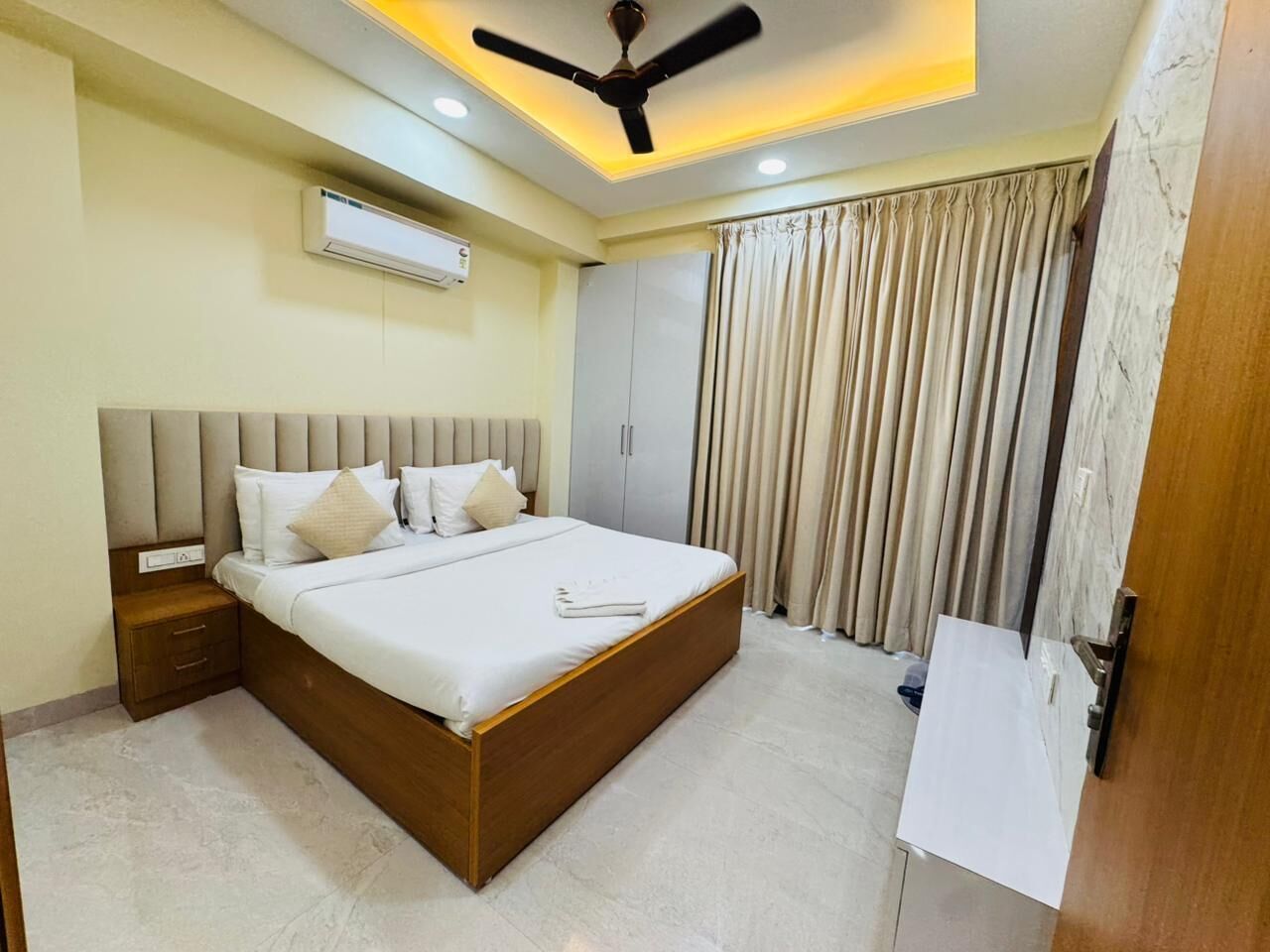 A bedroom with a bed, nightstand, wardrobe, and curtains.