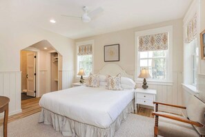 A bedroom with a large bed, two bedside tables, a chair, and a ceiling fan.