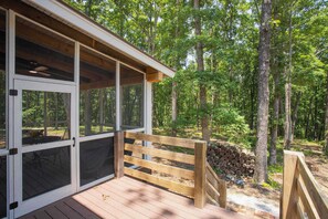 A wooden deck with a bench, a covered area with glass doors, and a forested background.