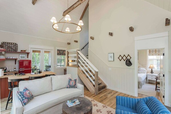 A spacious living room with a sofa, a blue striped chair, a wooden coffee table, and a staircase leading to another level.