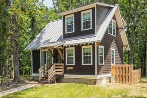A two-story cabin with a sloped roof, wooden deck, and a small staircase leading to the entrance. - Purple Martin: Secluded Forest Birdwatcher (McEwen)