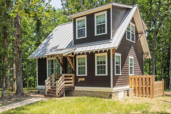 A two-story cabin with a sloped roof, wooden deck, and a small staircase leading to the entrance.