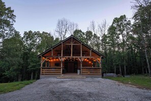 A wooden cabin with a porch, surrounded by trees.
