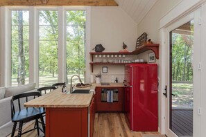 A compact kitchen with a wooden island, a red refrigerator, and a dining area with black chairs.