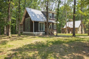 A cabin with a large front porch, a staircase leading to the upper level, and a second cabin in the background.