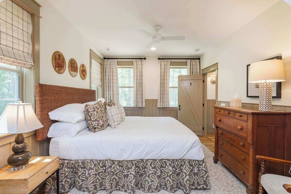 A bedroom with a large bed, a wooden dresser, a nightstand, and a ceiling fan.