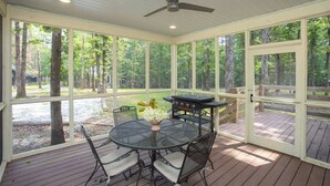 Een overdekt terras buiten, met een ronde tafel en stoelen, een barbecue en een plafondventilator.