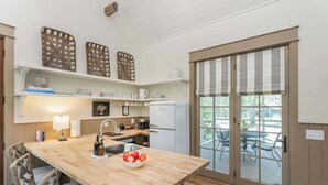 Een keuken met een houten kookeiland, barstoelen, een schaal met fruit en uitzicht door een schuifdeur naar een terras.