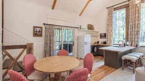 A cozy kitchen with a wooden table and chairs, a refrigerator, and a window with curtains.