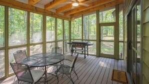 A covered porch with a table and chairs, a grill, and large windows offering a view of the forest.