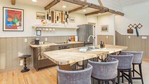 Una cocina con vigas de madera, una isla central con sillas y diversos electrodomésticos.