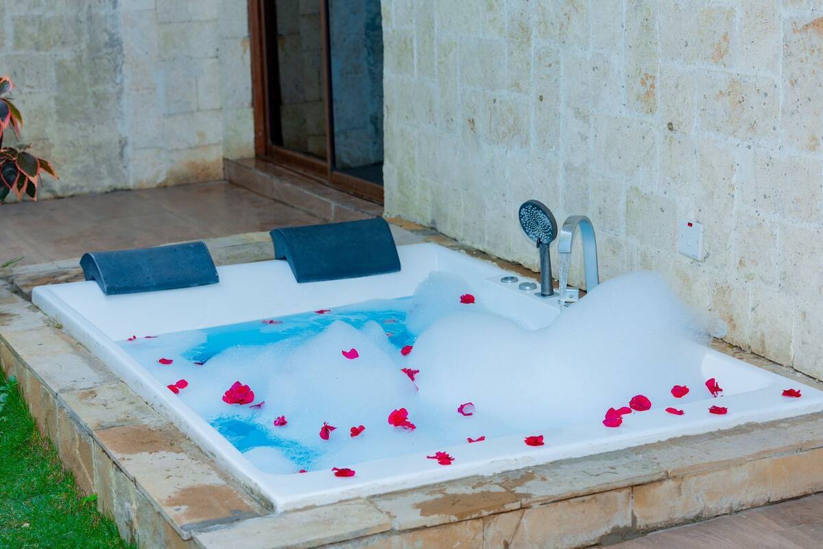 A spa tub with rose petals, a shower head, and two towels.