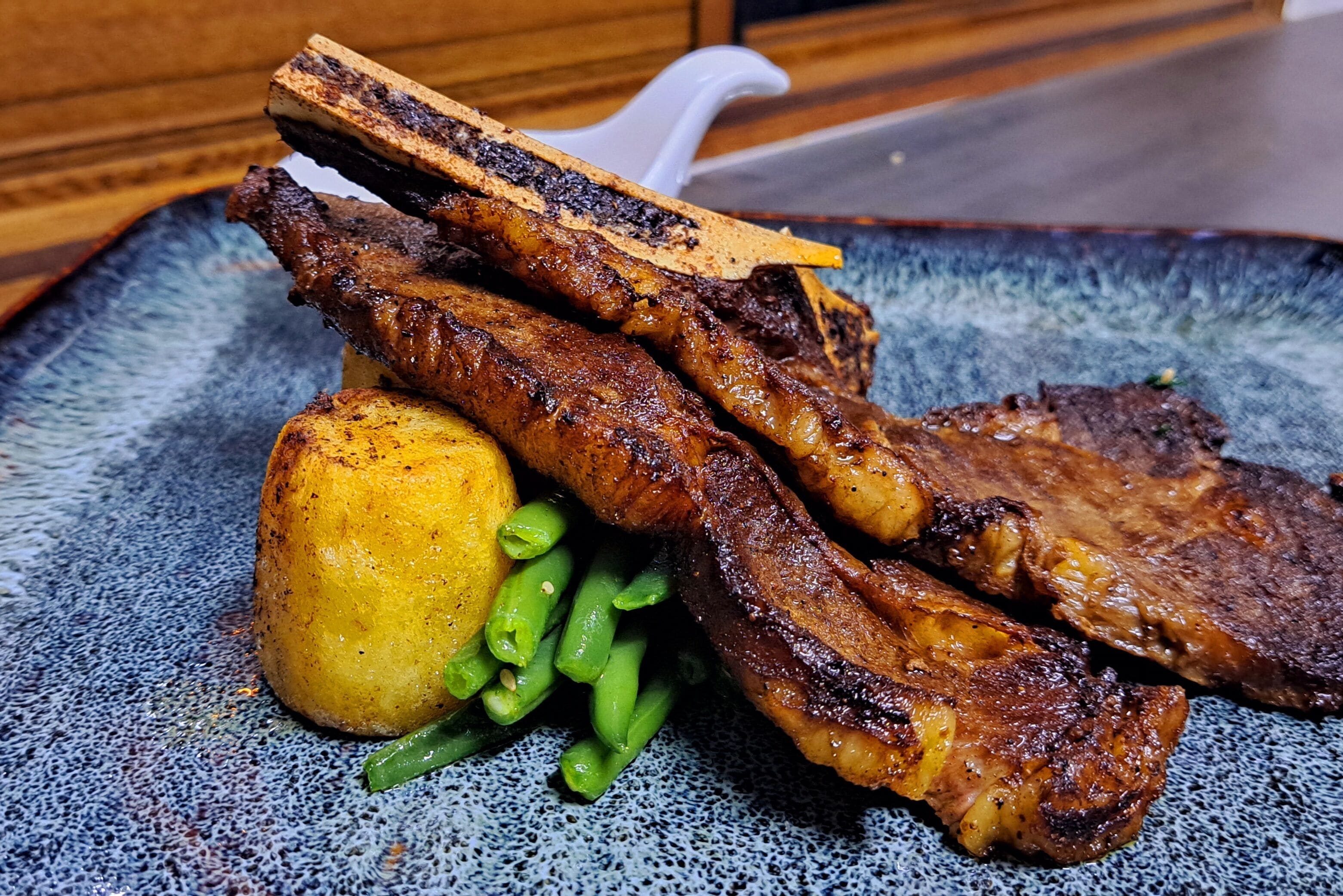 Une assiette contenant de la viande grillée, une pomme de terre et des haricots verts.