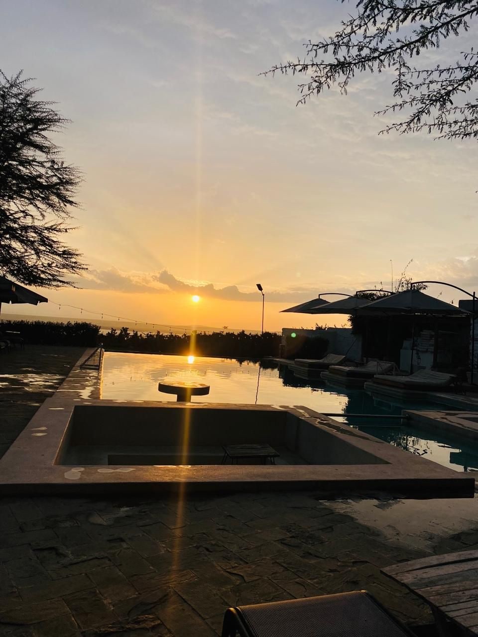 A swimming pool with a sunken seating area, surrounded by lounge chairs and umbrellas, with a sunset in the background.