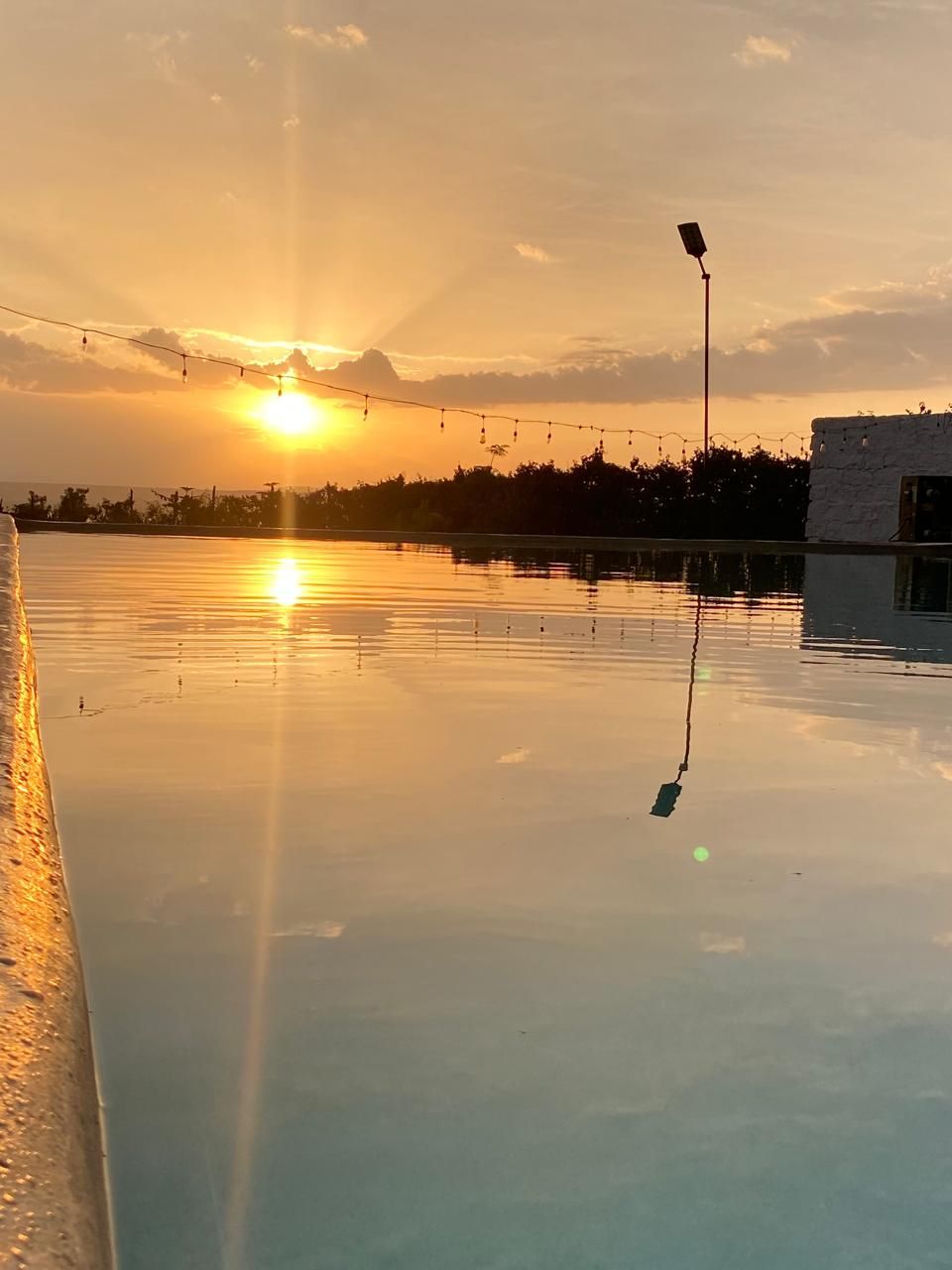 Una piscina en la azotea con vista al atardecer, luces colgantes y un farol.