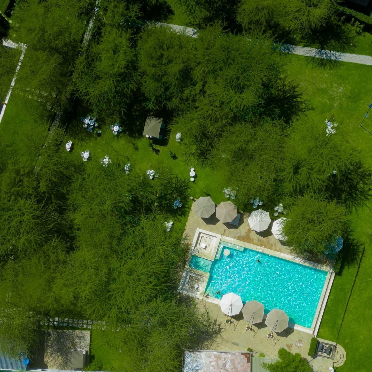 Vue aérienne d’une propriété dotée d’une piscine, entourée d’arbres et d’un espace de détente extérieur.