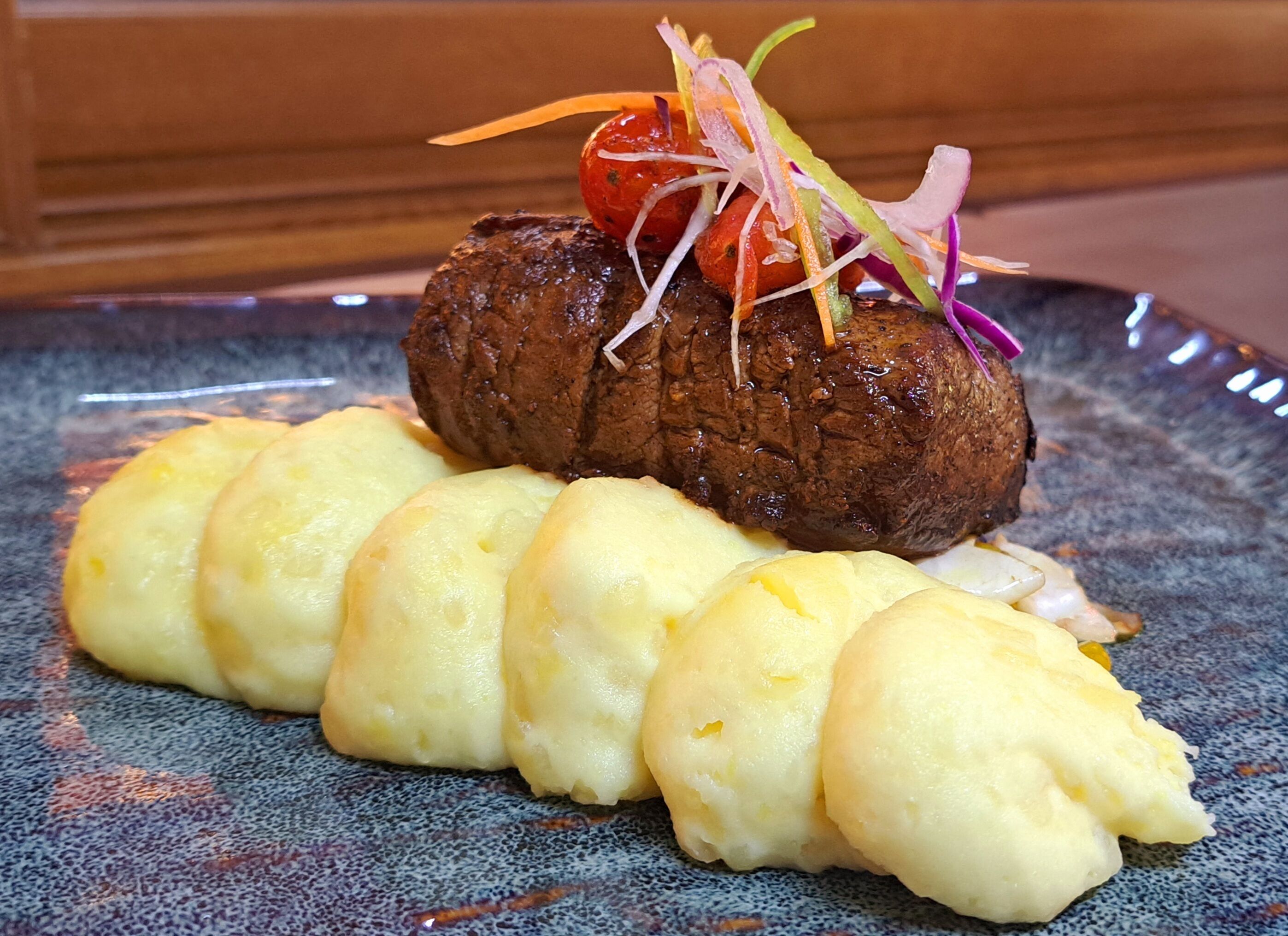 Ein Teller mit einem Steak, belegt mit einer Kirsche und Gemüse, dazu Kartoffelpüree.