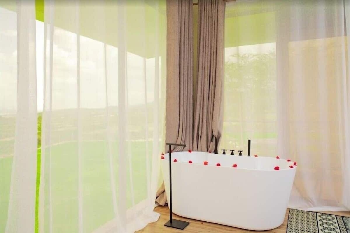 A room with a bathtub, sheer curtains, and a view of greenery.