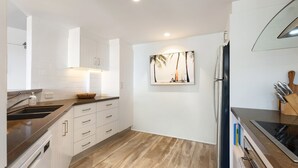 Una cocina moderna con armarios blancos, piso de madera, refrigerador de acero inoxidable y un cuadro colgado en la pared.