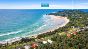 Vista aérea de una zona costera con playa, un faro y un cartel que indica 'Apartment 3 Surfside'.