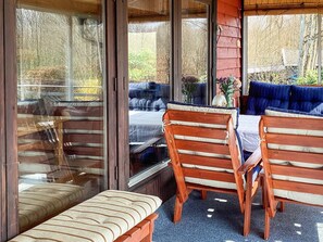 A cozy outdoor seating area with wooden benches and a table, surrounded by large windows offering a view of the outdoors. - 6 Person Holiday Home in Hjarnarp (Hjarnarp)