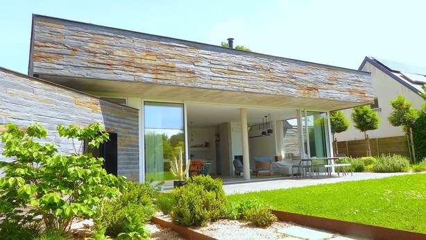 Une maison moderne avec une façade en pierre, un patio couvert et un jardin bien entretenu.