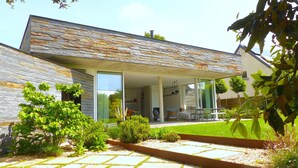 Une maison moderne avec une façade en pierre, un patio couvert et un jardin bien entretenu.