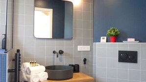Une salle de bain moderne avec un lavabo rond, un miroir, un porte-serviettes avec des serviettes pliées et une plante en pot accrochée au mur.