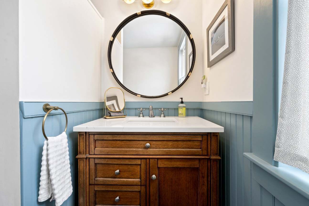 A bathroom with a wooden vanity, a round mirror, and a white sink.