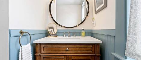 A bathroom with a wooden vanity, a round mirror, and a white sink.