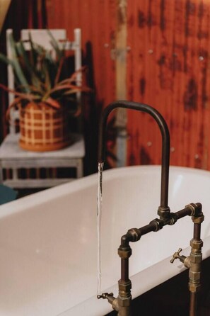 Eine weiße Badewanne mit einem alten Wasserhahn und einer Pflanze im Hintergrund.