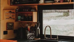 A compact kitchen with a microwave, tea shelf, and a window with a view of the outdoors.