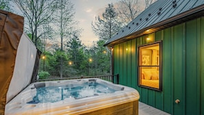 Un jacuzzi en una terraza de madera con vistas a un edificio verde y árboles.