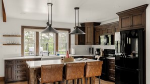 Una cocina moderna con una isla grande, taburetes de bar, lámparas colgantes y armarios de madera.