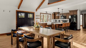 Un comedor amplio con una mesa y sillas de madera, una cocina con electrodomésticos modernos, y un techo alto con vigas a la vista.