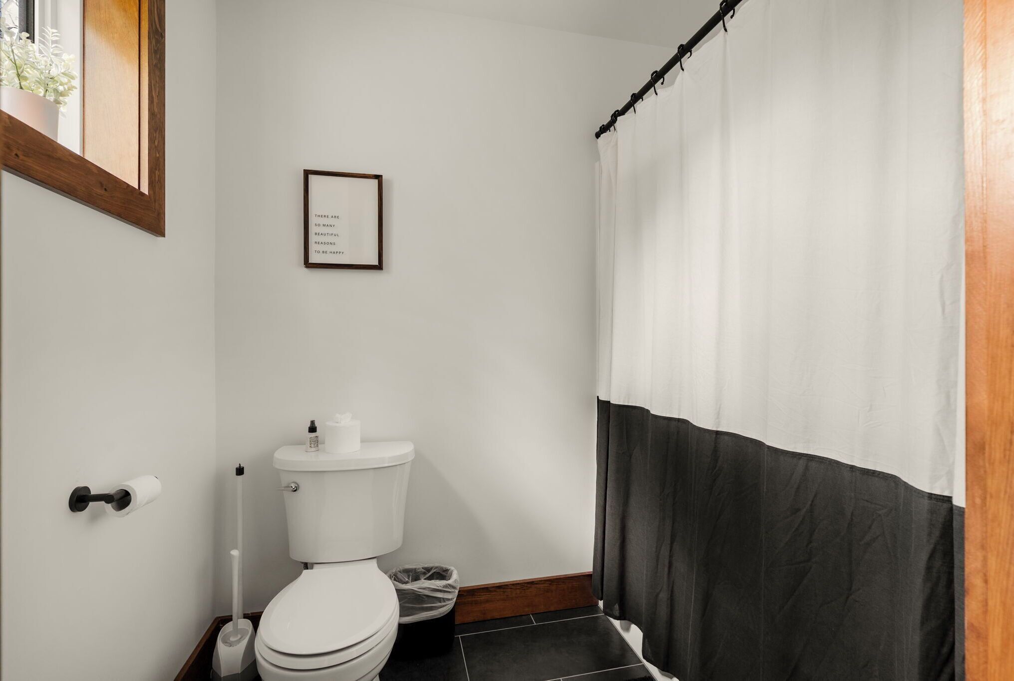 Een badkamer met toilet, een lijst met een citaat aan de muur en een douchegordijn.