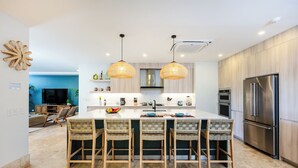Cocina moderna con una isla central, taburetes de bar, luces colgantes y un refrigerador integrado.
