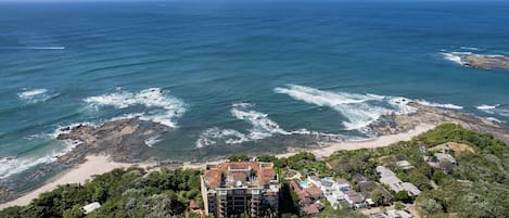 A coastal hotel with a pool, surrounded by lush greenery and rocky terrain.