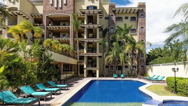 Un hotel con piscina, varios balcones y palmeras.