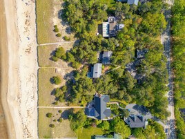 Vista aérea de una zona residencial con casas rodeadas de árboles, una playa y una carretera.
