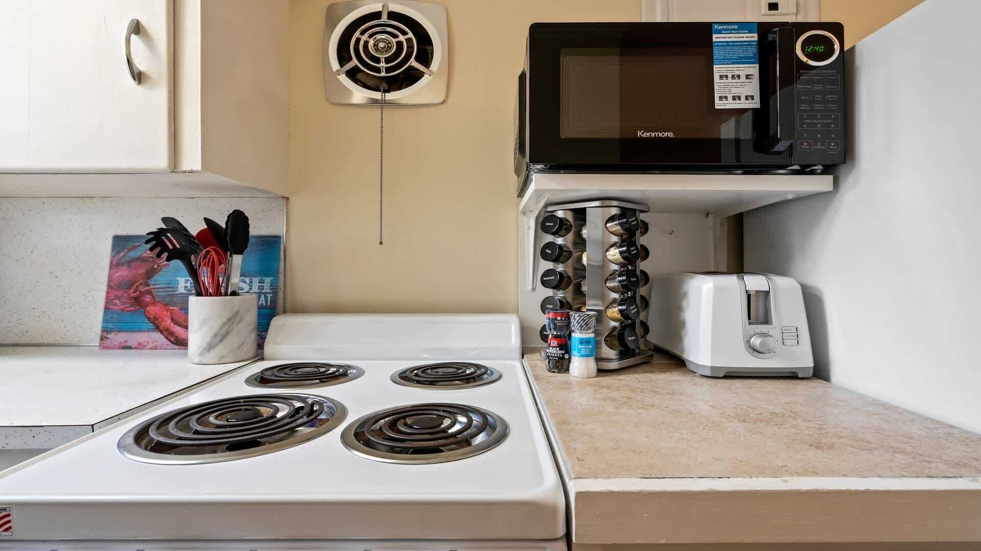 Een keuken met een fornuis, magnetron, broodrooster en kruidenrek.