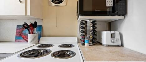 A kitchen with a stove, microwave, toaster, and spice rack.